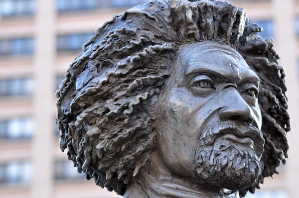 Image is a close-up of a gray statue of Frederick Douglass from the neck up.