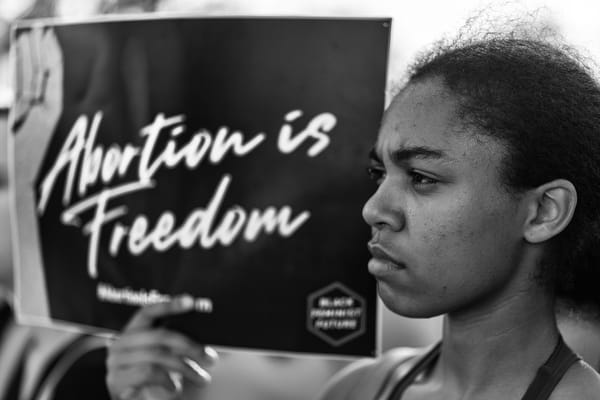 Black and white photo of young Black woman holding up a sign that reads "Abortion is Freedom."